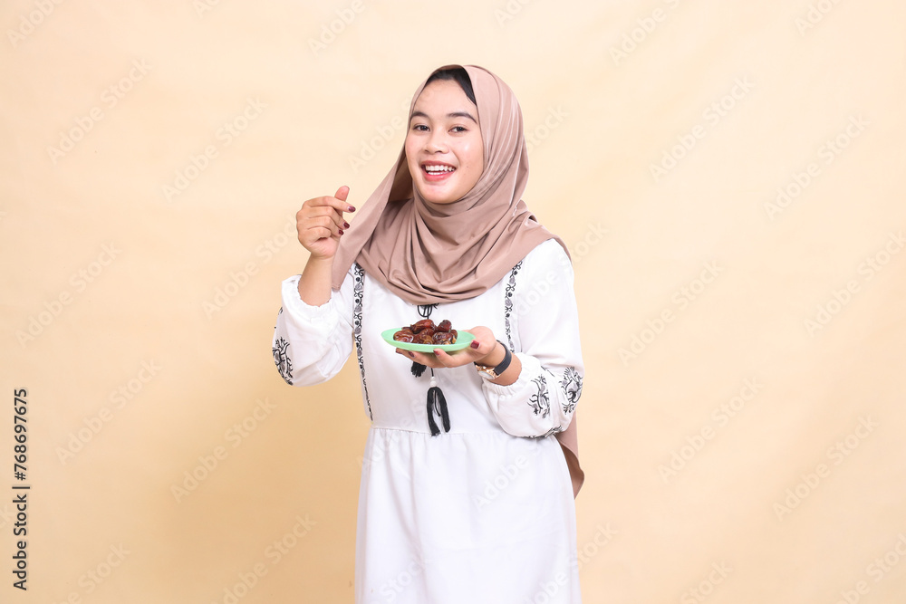 A beautiful indonesia Muslim woman wearing a hijab smiles cheerfully as a sign of love and brings some dates for the meal and breaking the fast. used for advertising, health, Eid and Ramadan