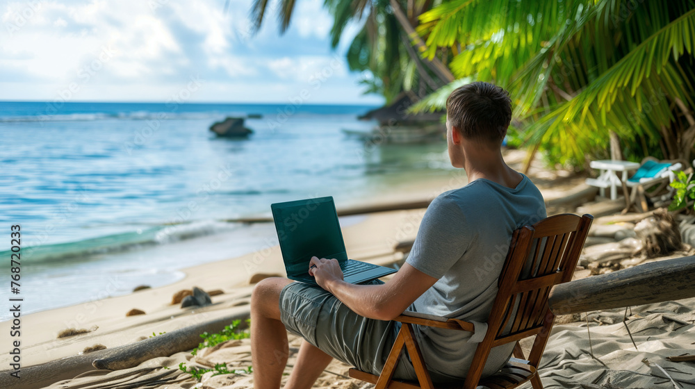 A person working remotely on a laptop under the shade of palm trees, with the serene blue ocean in the background.