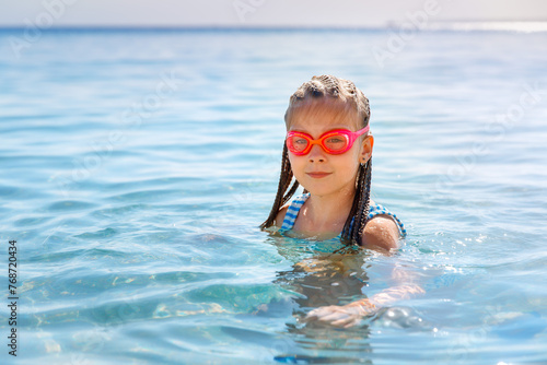  Blonde girl with pink goggles swimming in the sea, looking at the camera, smiling
