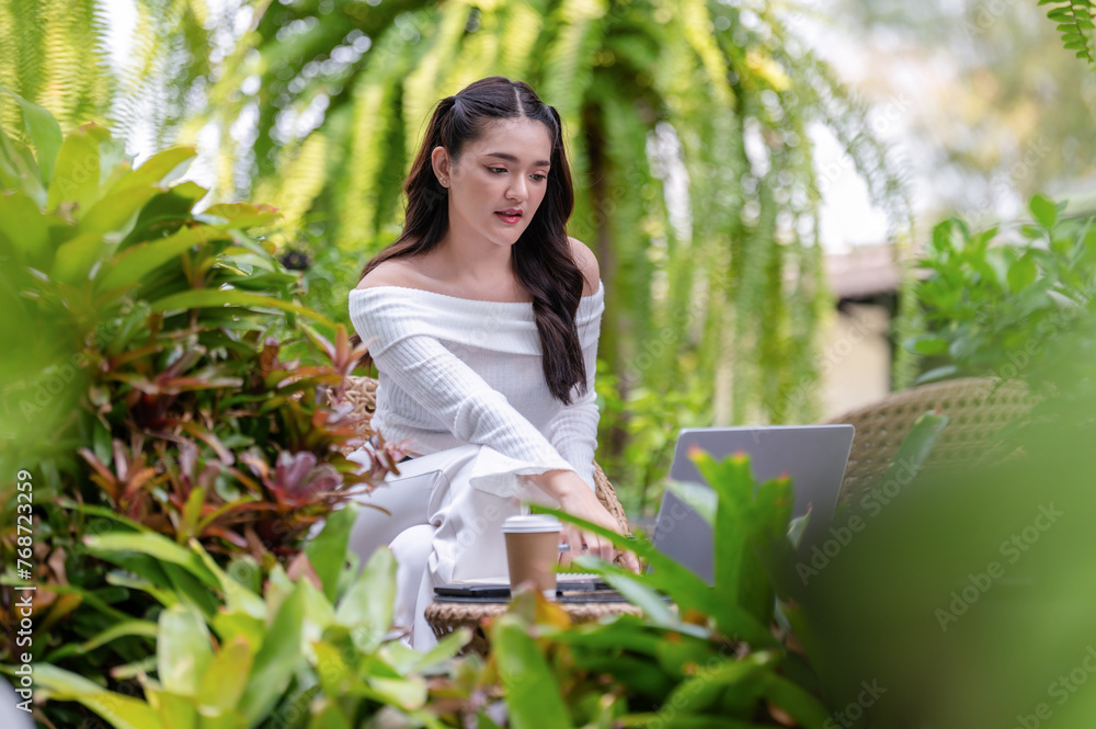 A happy young woman enjoys remote work on her laptop, comfortably seated outdoor of cafe with a coffee. A happy young woman enjoys remote work on her laptop, comfortably seated outdoor of cafe with a coffee.