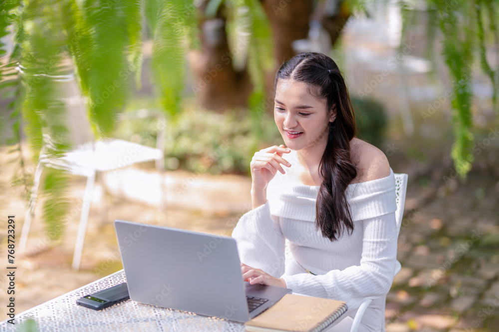 A happy young woman enjoys remote work on her laptop, comfortably seated outdoor of cafe with a coffee. A happy young woman enjoys remote work on her laptop, comfortably seated outdoor of cafe with a coffee.