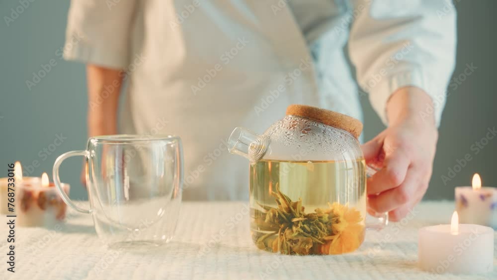 person close-up hand pour white blooming tea into a cup mug, beautiful natural drink yellow flower opens in hot water, fresh green leaves, tea ceremony. transparent glass teapot, candles burning 4k person close-up hand pour white blooming tea into a cup mug, beautiful natural drink yellow flower opens in hot water, fresh green leaves, tea ceremony. transparent glass teapot, candles burning 4k