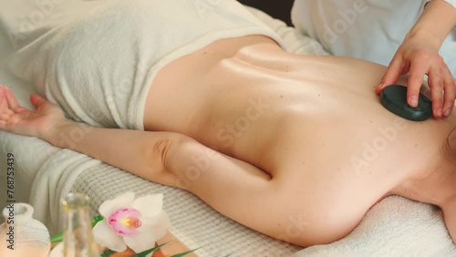 hands close-up female masseur puts black flint stones on back adult girl. happy young woman customer enjoying relaxing hot stone massage therapy at spa salon. Healthy lifestyle body care concept, 4k photo