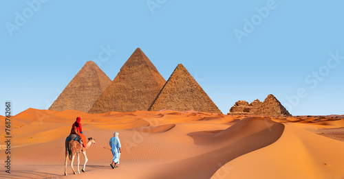 Camels in Giza Pyramid Complex - A woman in a red turban riding a camel across the thin sand dunes - Cairo  Egypt