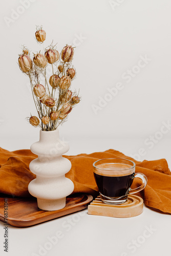 Stylish ceramic vase with dry flower bouquet, linen cloth and cup of coffee on cup coaster. Cozy still life composition for poster, interior home decoration