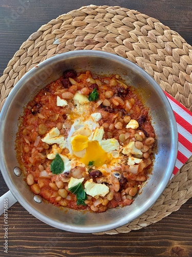 shakshuka, white beans in tomatoes, fried eggs with beans and tomatoes, wicker placemat