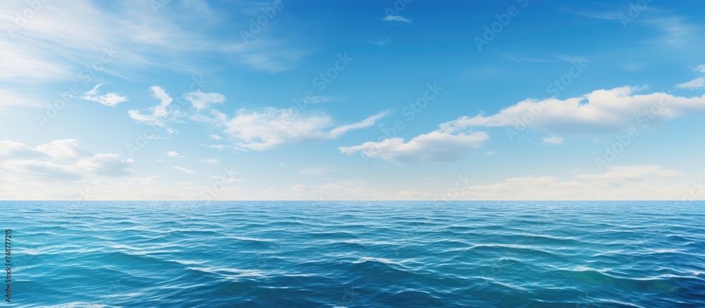 Fototapeta premium A serene blue ocean under the clouds, with gentle waves on the water surface and a clear horizon against the sky
