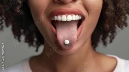 A close-up of a smiling woman with a tongue piercing showcasing her white teeth and the small round stud in her tongue. photo