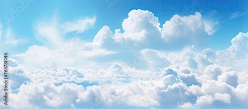 Fluffy white cumulus clouds float peacefully in the vast expanse of the clear blue sky above