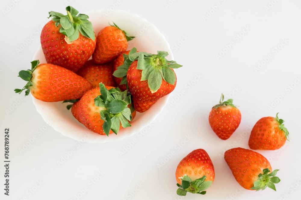 some strawberries in a white bowl and another on a white table some strawberries in a white bowl and another on a white table