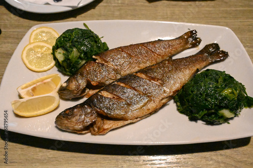 Grilled trout served on plate in restaurant. Tasty fish served with potato and spinach. Delicious roasted fish prepared for dinner. 
