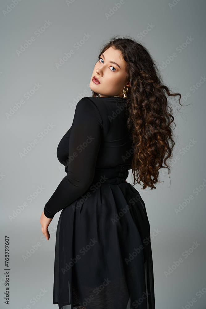 attractive curvy woman in black outfit looking to camera from behind back on grey background attractive curvy woman in black outfit looking to camera from behind back on grey background