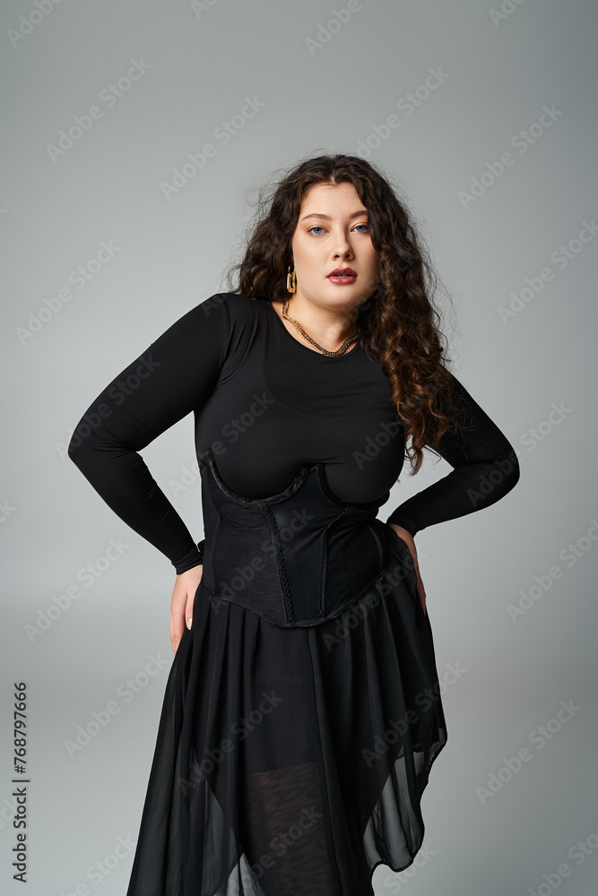 beautiful plus size young girl in black outfit posing with hands on hips on grey background beautiful plus size young girl in black outfit posing with hands on hips on grey background