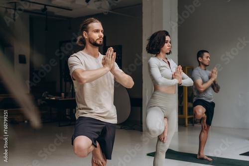 Calm people meditating together while balancing on one leg