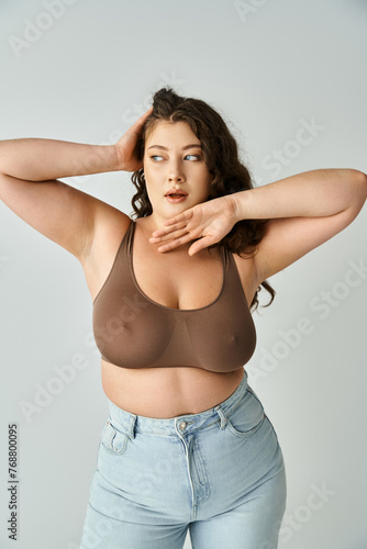 attractive plus size young woman in brown bra and blue jeans looking to side and posing with hands