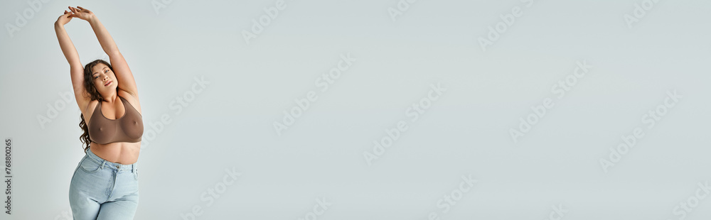banner of cheerful curvy woman in brown bra and blue jeans with curly hair putting hands to up - obrazy, fototapety, plakaty 