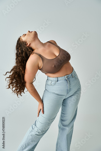 alluring plus size woman in brown bra and blue jeans with curly hair putting head to behind