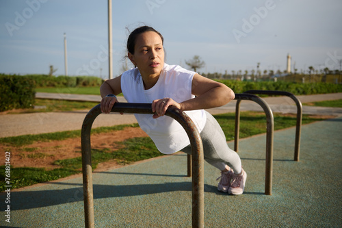 Young woman is engaged in fitness, stretching on sports field in city. Fitness woman working out doing push-ups in park