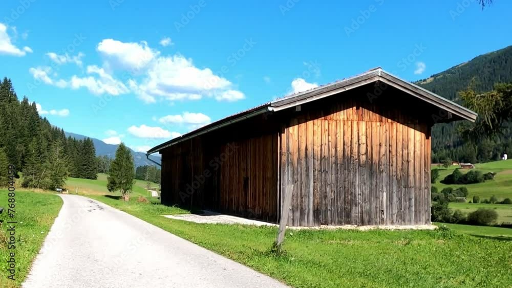 Beautiful view from a drive of a green field with wooden barn, trees, pathway, mountain Beautiful view from a drive of a green field with wooden barn, trees, pathway, mountain