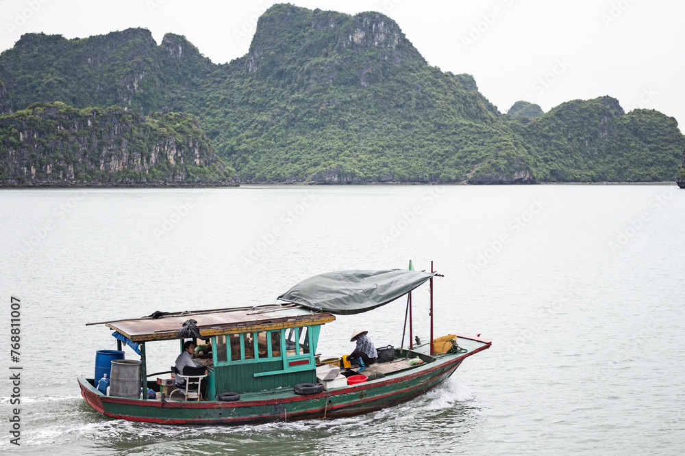 Fishing boat with people sailing on water near the mountains of Vinh Ha Long, Vietnam