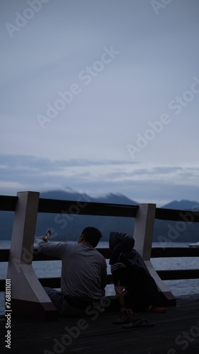 Couple enjoying a romantic moment, sitting on the shore of the beach during an evening sunset © Wirestock