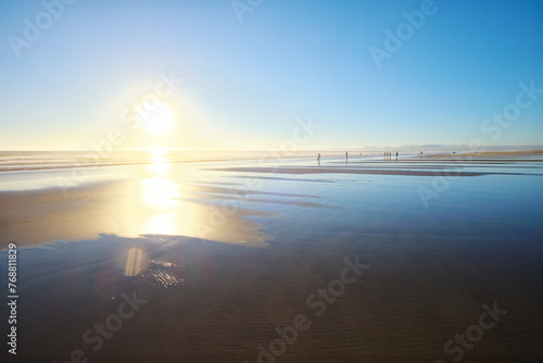 Atlantic ocean sunset with sun and surging waves at wide sand of Fonte da Telha beach, Costa da Caparica, Portugal