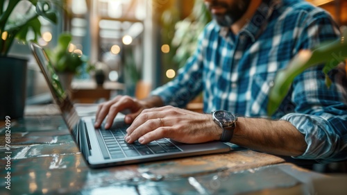 Man typing on laptop, focus on hands in cozy cafe