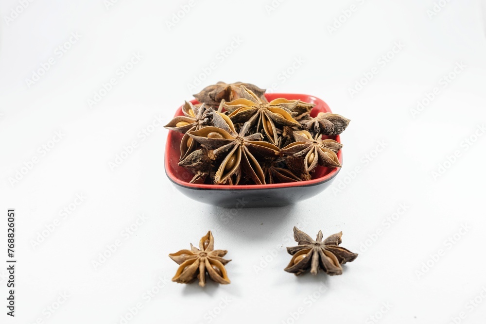 Close-up shot of a pile of star anise in a red bowl on a white background