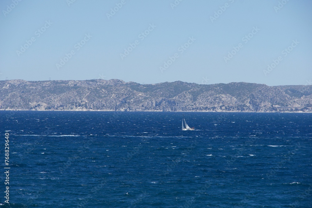 Sailboat gliding across a sparkling blue sea with mountains and a blue sky in the background Sailboat gliding across a sparkling blue sea with mountains and a blue sky in the background