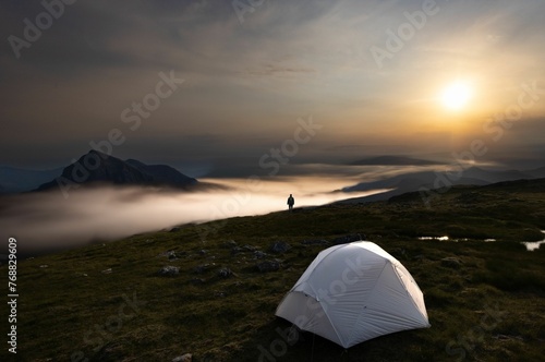 Adventure-seeking outdoorsman in front of a tent on a mysterious foggy mountainous terrain