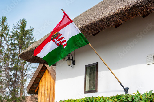 hungarian waving flag with crest placed on a traditional straw roof house