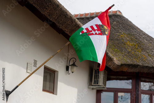 hungarian waving flag with crest placed on a traditional straw roof house