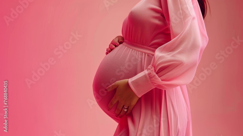 Exuding grace and serenity, a pregnant woman embraces her belly, draped in delicate pink attire. The soft hue adds to the elegance of her pregnancy journey, radiating warmth and femininity.