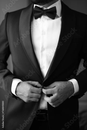 Young adult man wearing a formal tuxedo adjusting his black bow tie in a mirror