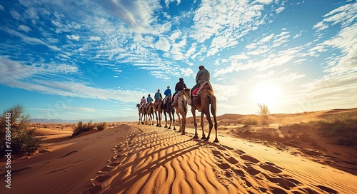 The group of people riding camels in the desert dunes, backlighting photo