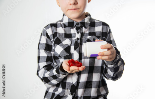 A girl in a checkered shirt holds chewable multivitamins in her palm for the growth and development of the child s immunity, close-up. The concept of a biological food additive for children's health photo