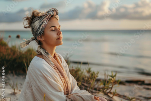 Beautiful young woman sitting on the beach mediating photo