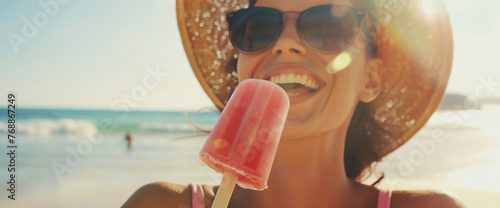 Beautiful happy woman on summer holiday wearing sun hat and eating a pink popsicle at the beach photo