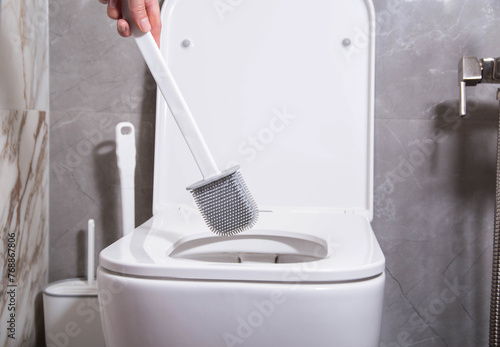 Modern silicone brush for cleaning the dirt of the wall-mounted toilet. Toilet care and hygiene concept, close-up photo