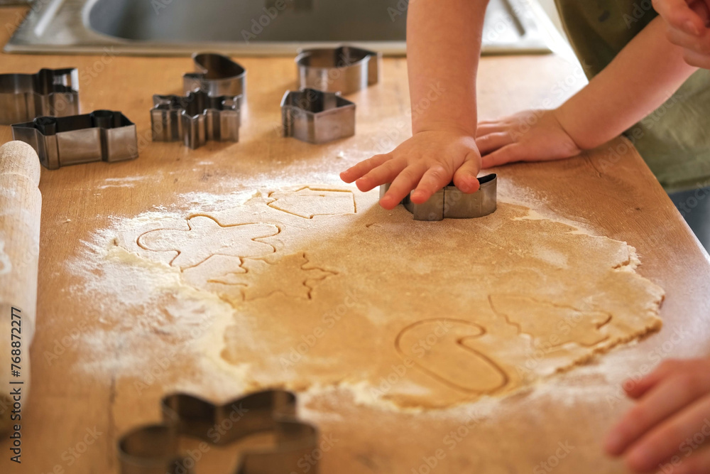 Children rolling out cookie dough with a wooden rolling pin on the kitchen countertop. Metal baking molds. Joy of childhood baking, family traditions, homemade treats. Siblings Helping to Mom together Children rolling out cookie dough with a wooden rolling pin on the kitchen countertop. Metal baking molds. Joy of childhood baking, family traditions, homemade treats. Siblings Helping to Mom together