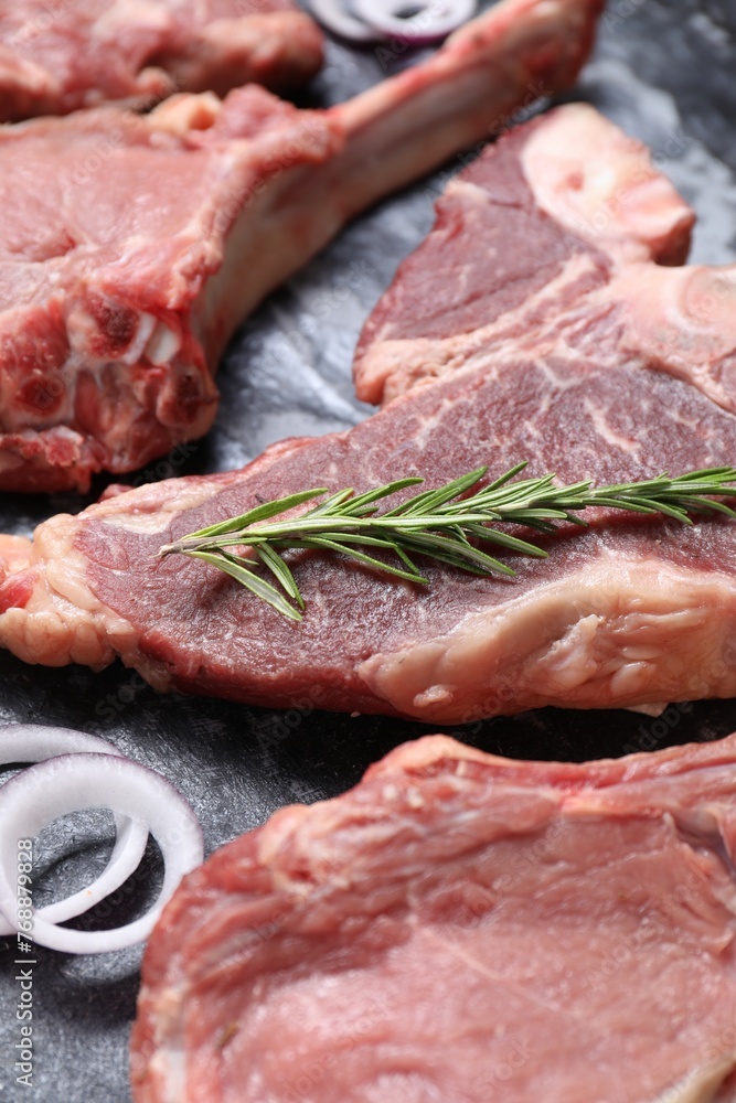 Fresh raw beef cuts with rosemary and onion on table, closeup Fresh raw beef cuts with rosemary and onion on table, closeup
