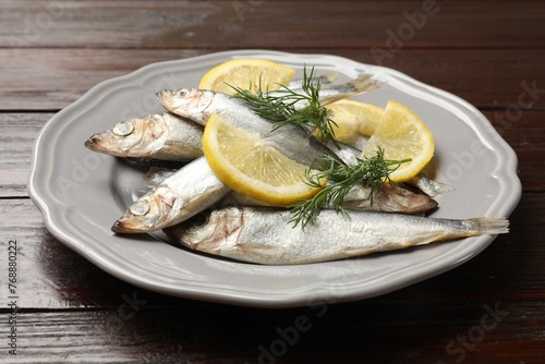 Fresh raw sprats, dill and cut lemon on wooden table, closeup