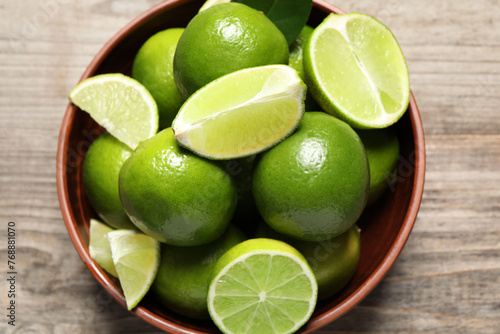 Tasty ripe limes in bowl on wooden table, top view