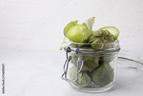 Fresh green tomatillos with husk in glass jar on light table, space for text photo