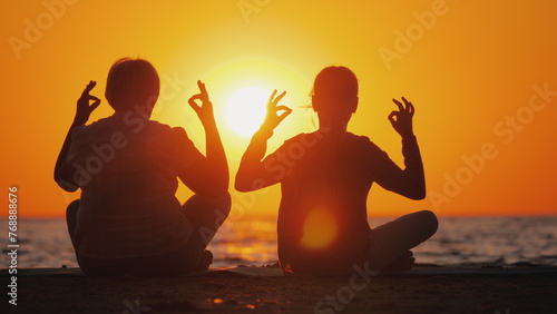 Grandmother and granddaughter meditate on the beach. Active and healthy seniors concept
