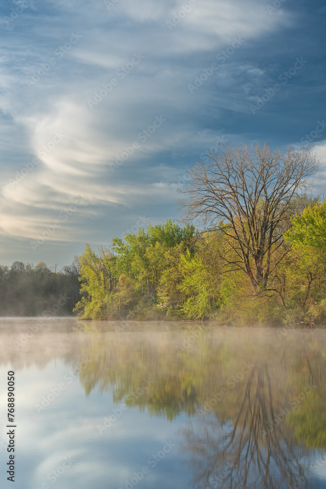 Foggy spring landscape at dawn of the shoreline of Jackson, Hole, Lake with mirrored reflections in calm water, Fort Custer State Park, Michigan, USA
