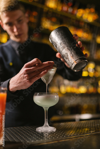 Barkeeper strains milk alcoholic cocktail through sieve to sort out large particles. Barman in uniform serves made cocktail
