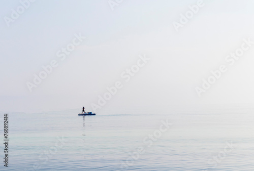 Shot of a man on a small catamaran boat by the horizon, which is hard to detect because of the fog and humidity. Outdoors