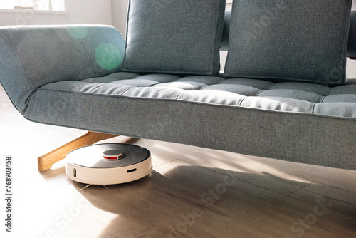 Robot vacuum cleaner on wooden floor under sofa