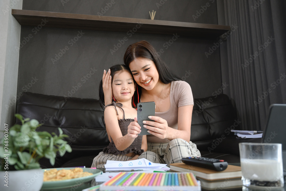 Beautiful Asian mother working at home and taking care of cute little daughter Beautiful Asian mother working at home and taking care of cute little daughter